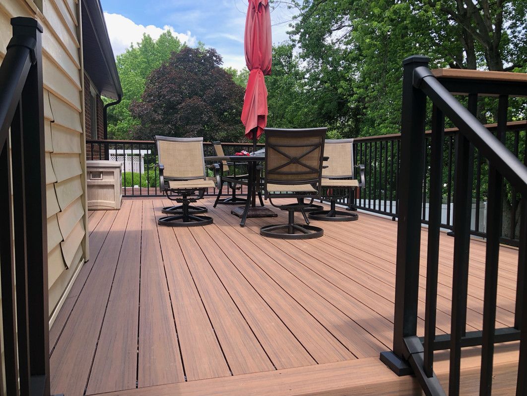 Wooden deck with patio furniture, red umbrella, and black railing.