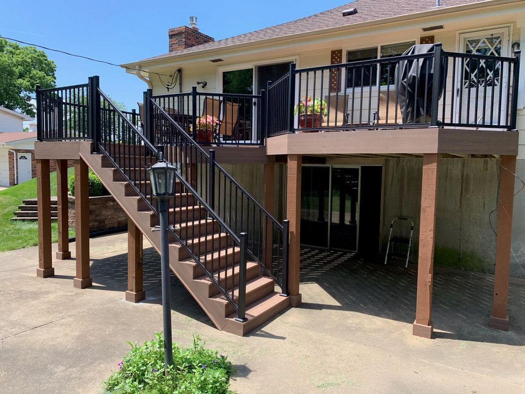 Raised deck with black railing and stairs attached to a two-story beige house.