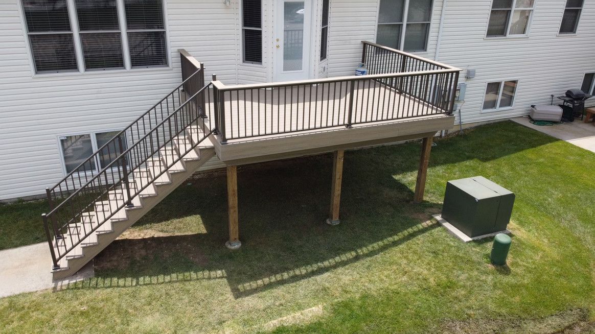 Deck with stairs attached to a house with a door, brown railing, and light brown boards.