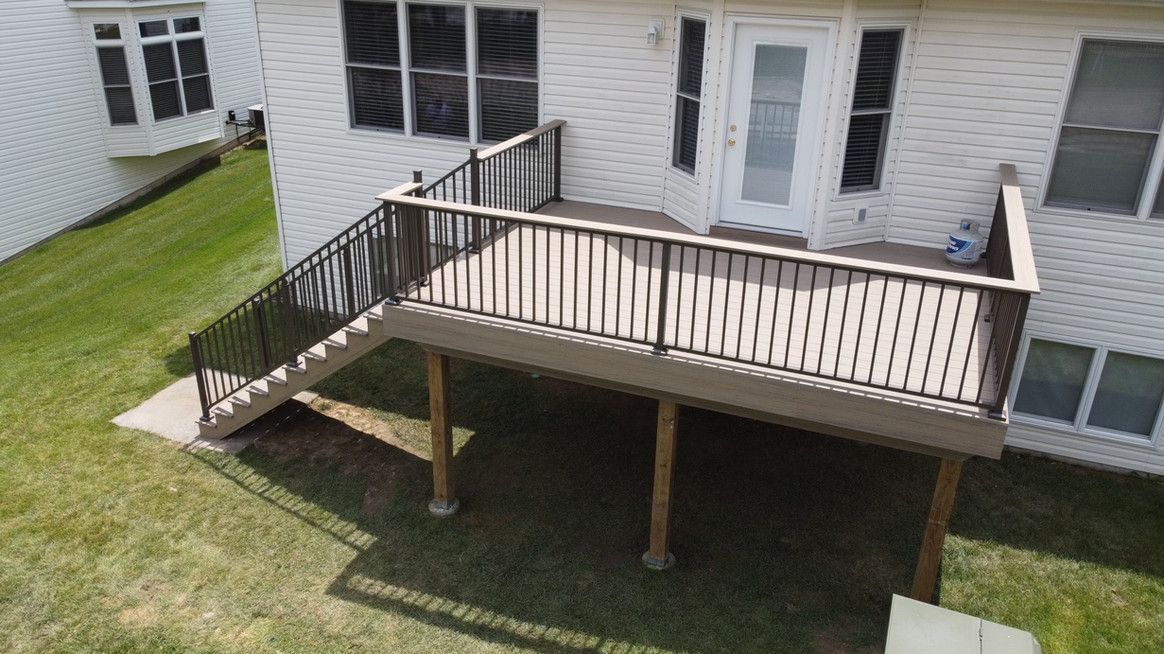 A backyard deck with stairs, surrounded by grass, leading to a white house with a glass-paned door.