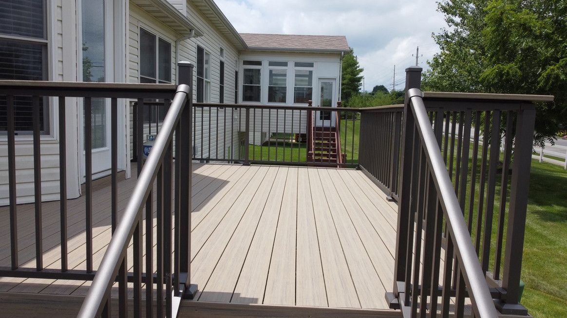 Deck with dark railings, light wood deck boards, and a house in the background on a sunny day.