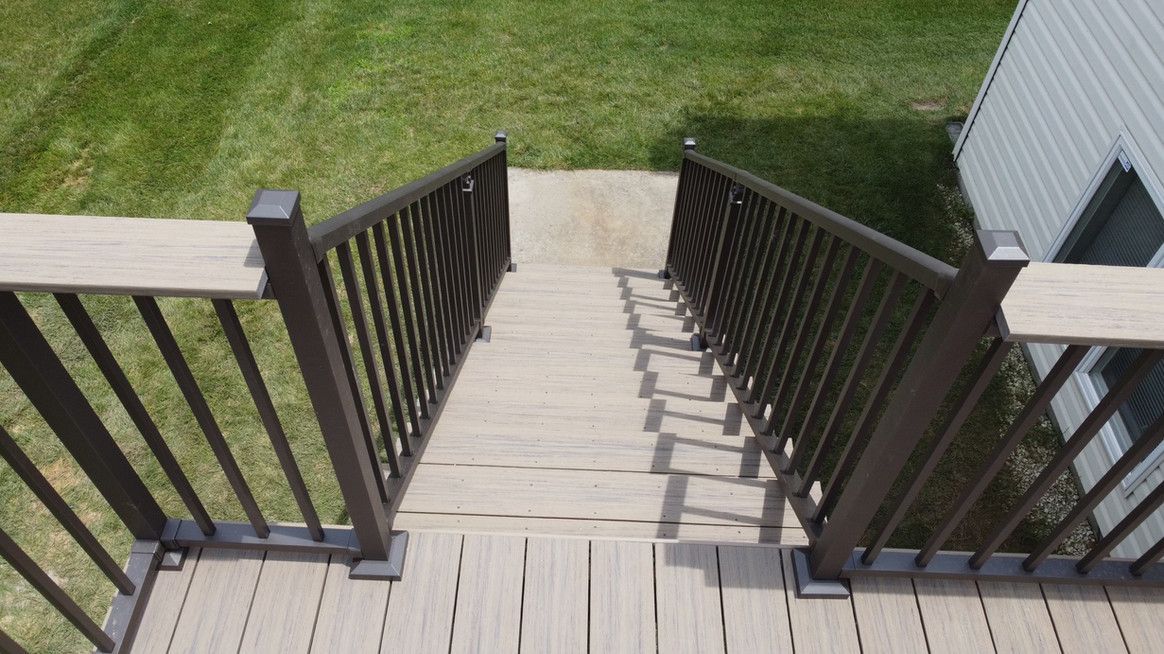 Wooden deck stairs leading down to grass. Brown railings with light-colored steps.