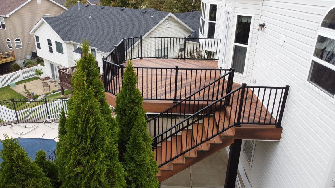 A multi-level wooden deck with black railings and stairs attached to a white house.