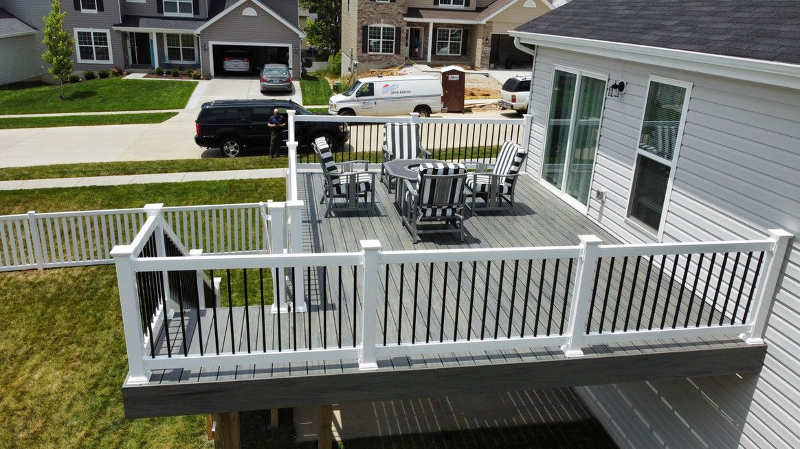 Elevated deck with white railing, black spindles, and patio furniture overlooking a residential neighborhood.