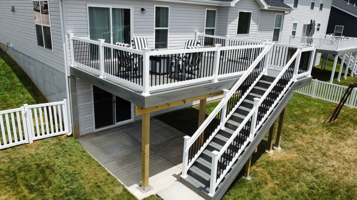 A multi-level deck with stairs and white railing attached to a house with black sliding doors.