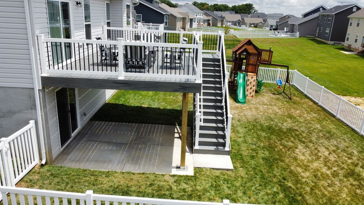 Backyard deck with stairs leading down to a lower patio. A child plays on a nearby playset.