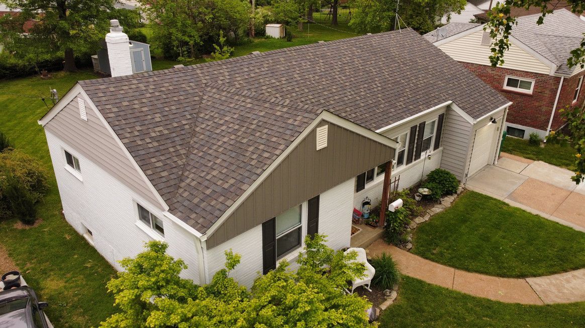 Gray house with a brown roof and a white garage, viewed from above, with green lawn.