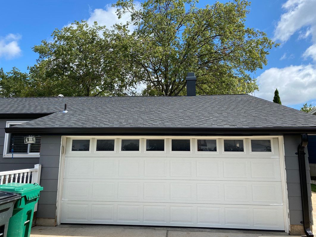 White garage door on a gray building under a dark roof, with a green bin on the left.
