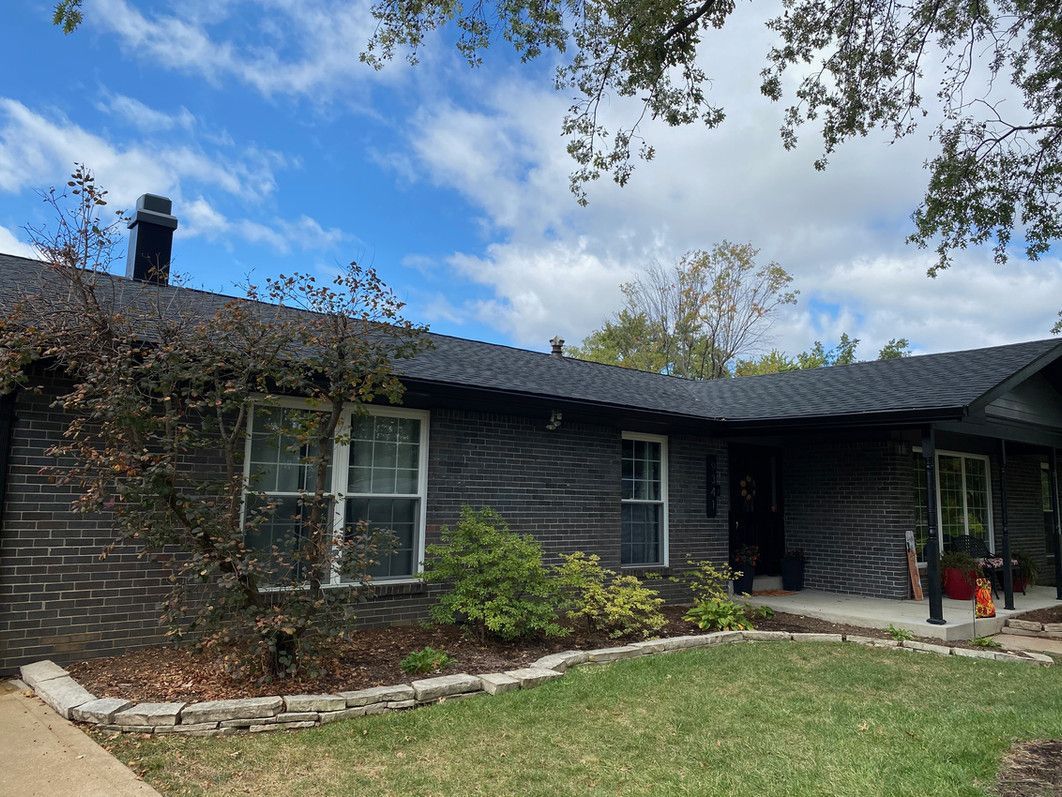 Dark-colored house with black roof, windows, and chimney. Landscaping in front of a blue sky.