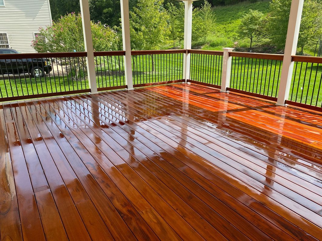 Wooden deck with glossy finish, surrounded by white columns and green railing, overlooking a lush backyard.