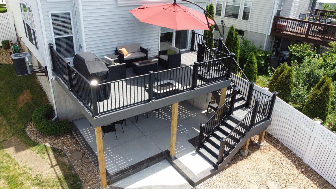 Two-tiered outdoor deck with black railing, red umbrella, and patio furniture. Grey concrete on bottom tier.