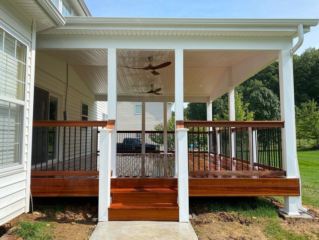 Covered porch with wood deck and railings, white pillars, and ceiling fans.
