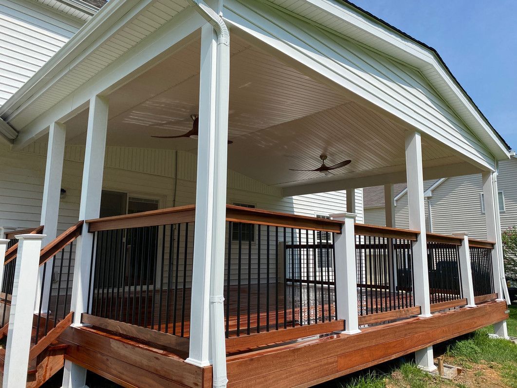 Covered wooden deck with black railings and white pillars, attached to a white house.