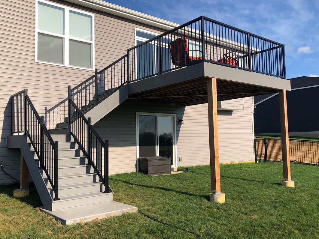 Gray deck with black railings and stairs. Wooden supports. Backyard with green grass.