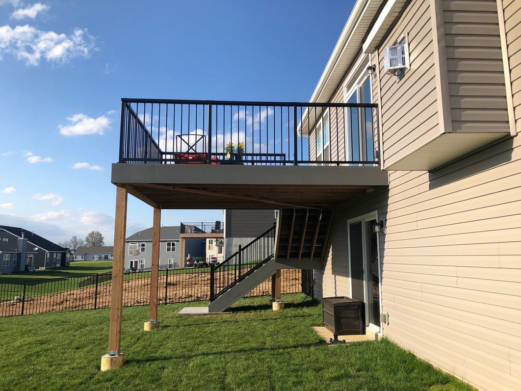 Wooden deck with black railing, stairs, and grass in a yard.