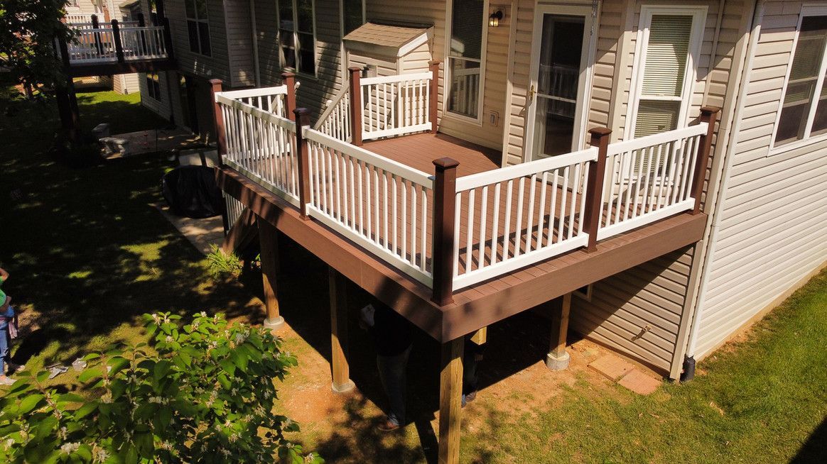 Brown and white deck with railings on a house with siding, surrounded by grass and trees.