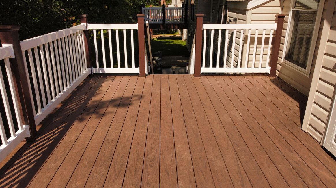 Wooden deck with white railing, brown posts, leading to steps, sunny day.