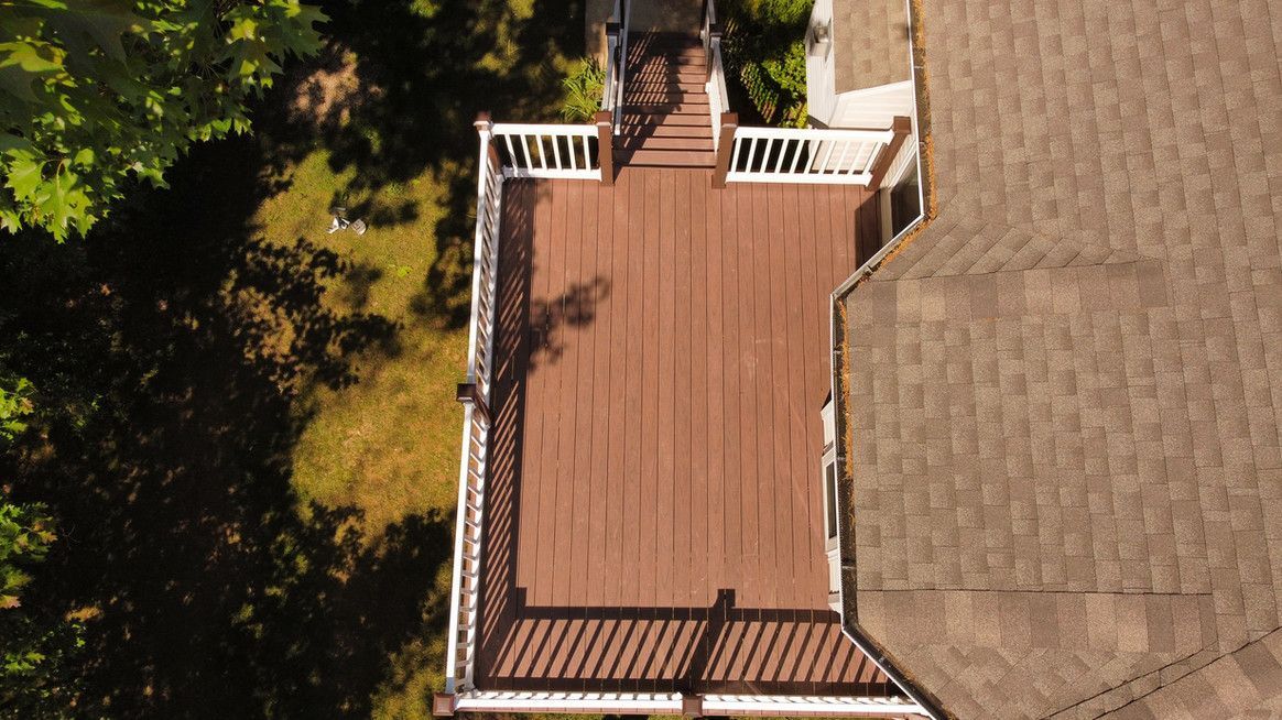 Overhead view of a brown wooden deck with white railing, connected to a house with brown shingles.