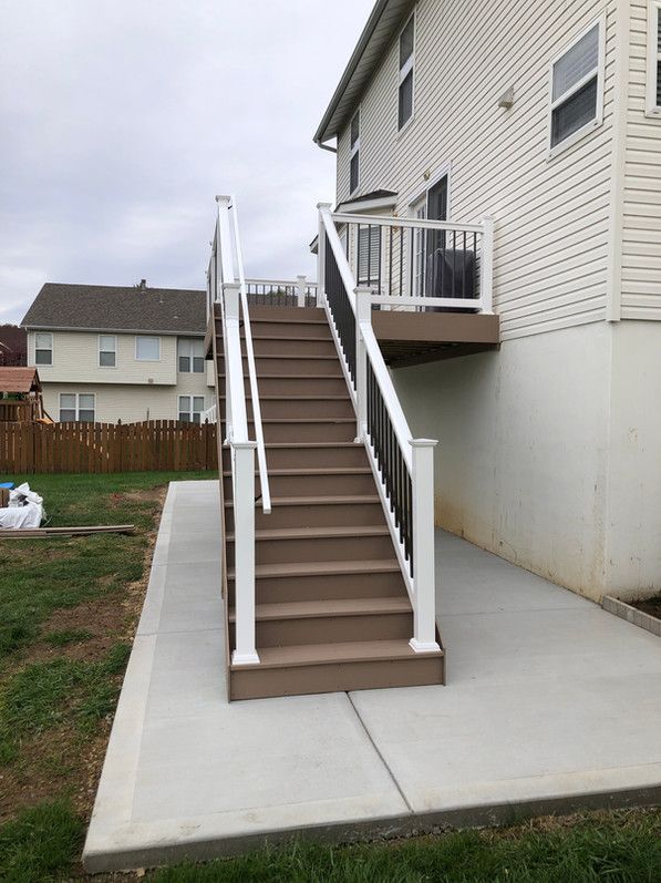 Composite stairs with white and black railings leading to a deck, set against a two-story beige house.