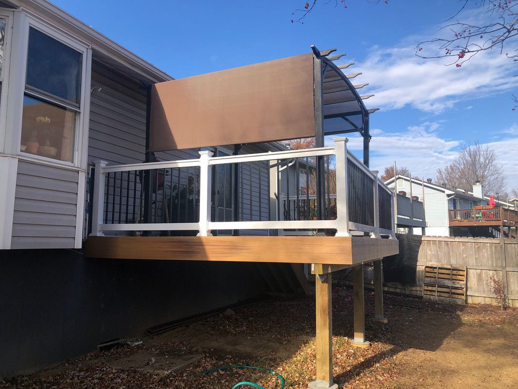 Deck with brown pergola and shade, white railing, attached to a gray house.