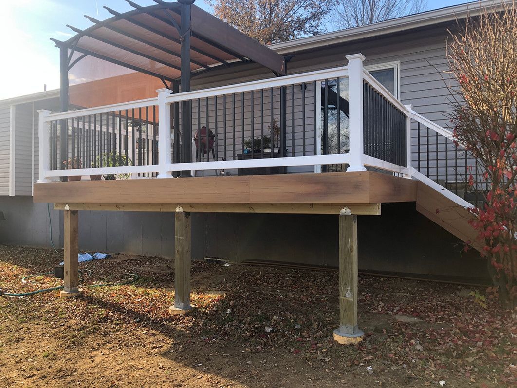 Wooden deck with white railing, black spindles, and a pergola attached to a house with a blue sky.