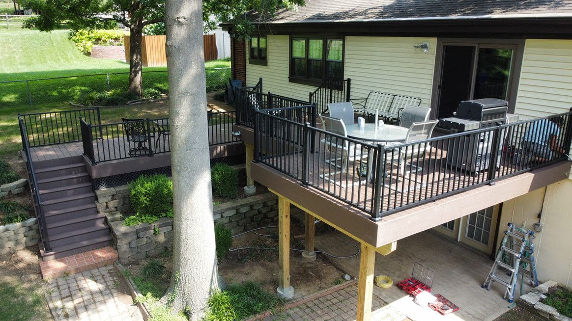 Multi-level decks on a house with black railings, outdoor furniture, and a grill. Stairs lead to the lower deck.