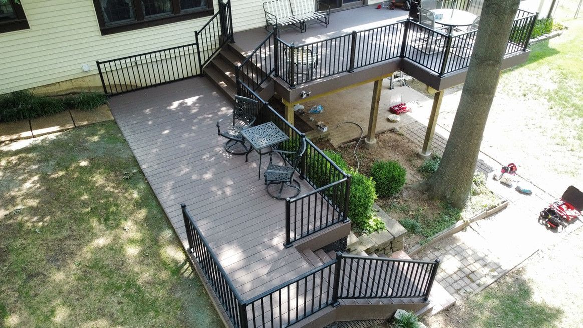Composite deck with black railings and steps next to a house, outdoor seating on lower level, yard.