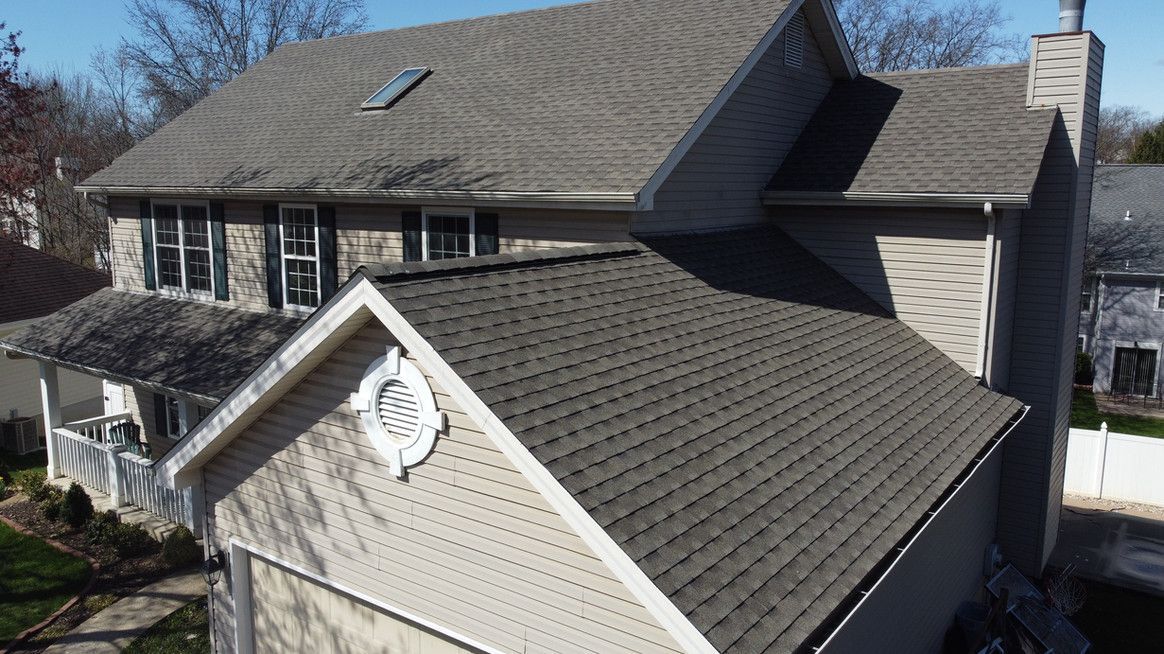 A two-story house with a tan exterior and a gray roof on a sunny day.