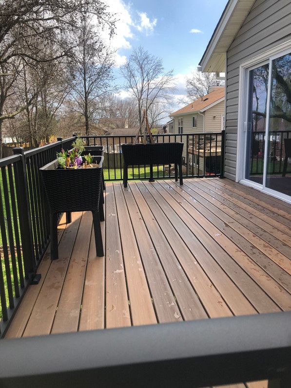 Deck with black railing, brown composite decking, and two black planters. Sliding glass door visible.