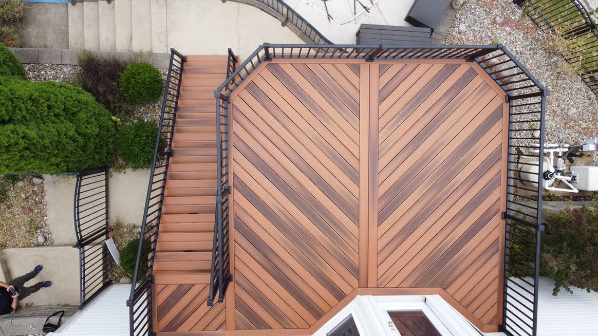 Overhead view of a wooden deck with diagonal planks, stairs, and black railing.