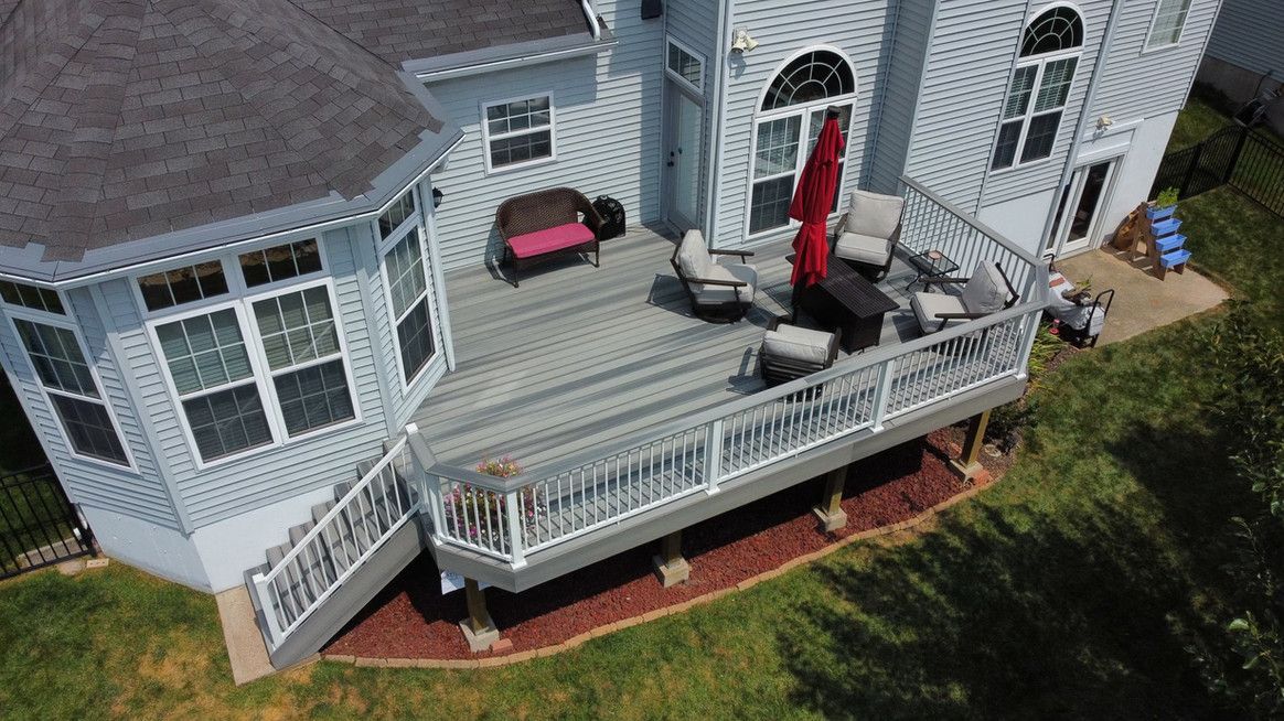 Elevated gray deck with seating, red umbrella, and a two-story house on a grassy lawn.