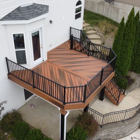 Elevated wooden deck with black railings and steps leading to a lower level near a house.