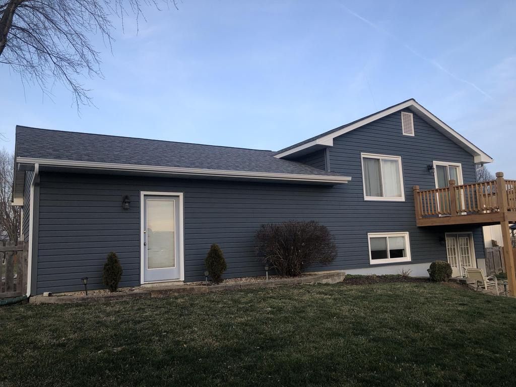 Blue-sided house with a small deck and a patch of brown grass under a cloudy blue sky.