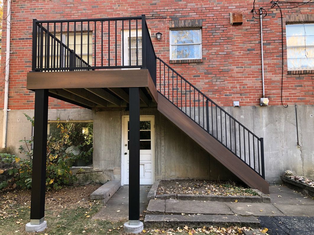 Composite deck with black railing and stairs against a brick building.