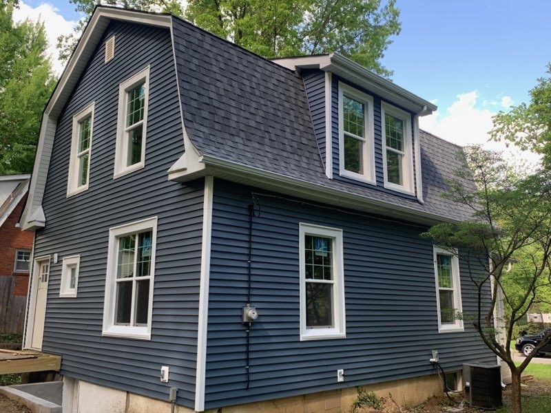 Blue-sided house with white window frames and a dark roof; set in a yard with trees.