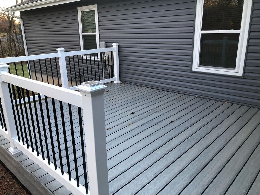Gray composite deck with white railings and black balusters against a gray house with two windows.