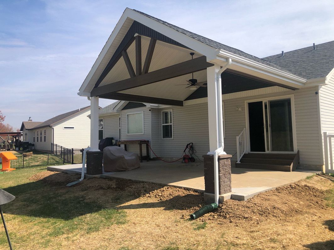 Covered patio with white columns, brown beams, and a concrete floor extending from a house.