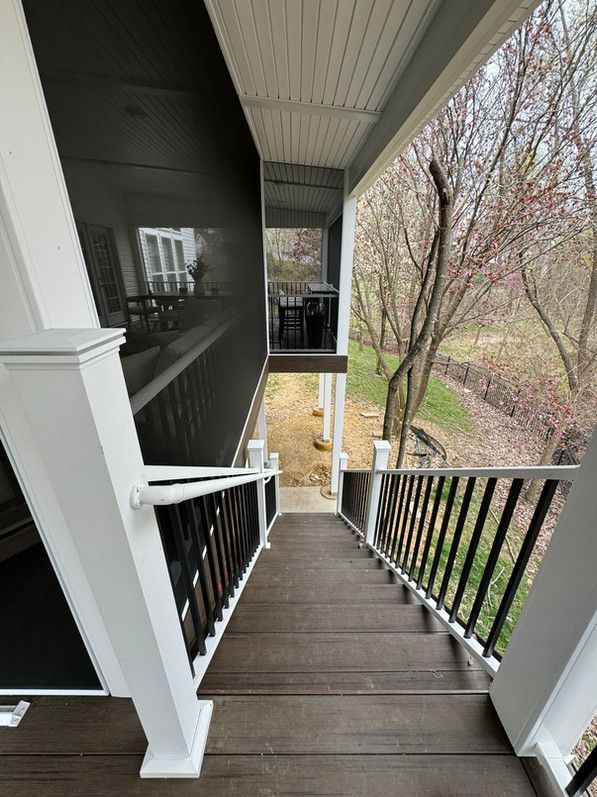 Stairs leading down from a porch with black railing and white columns. View of trees and backyard.