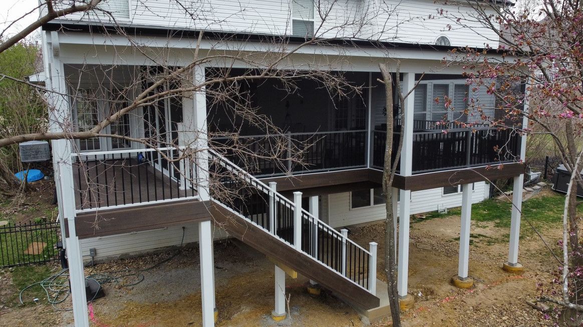 A two-story white house with a screened-in porch and elevated wooden deck. Trees frame the house.