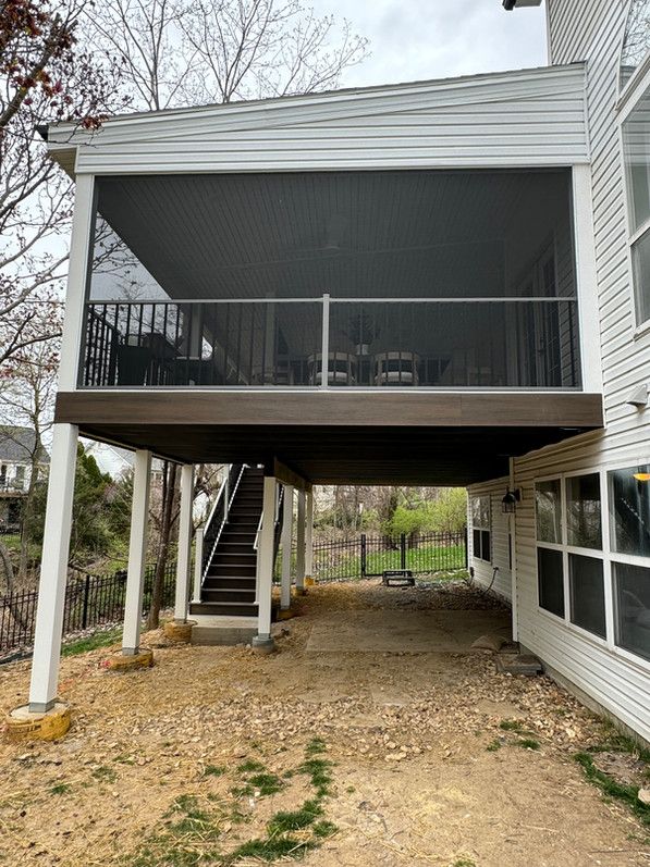 Screened-in porch with stairs leading to a ground-level area. Beige gravel ground, white house exterior.