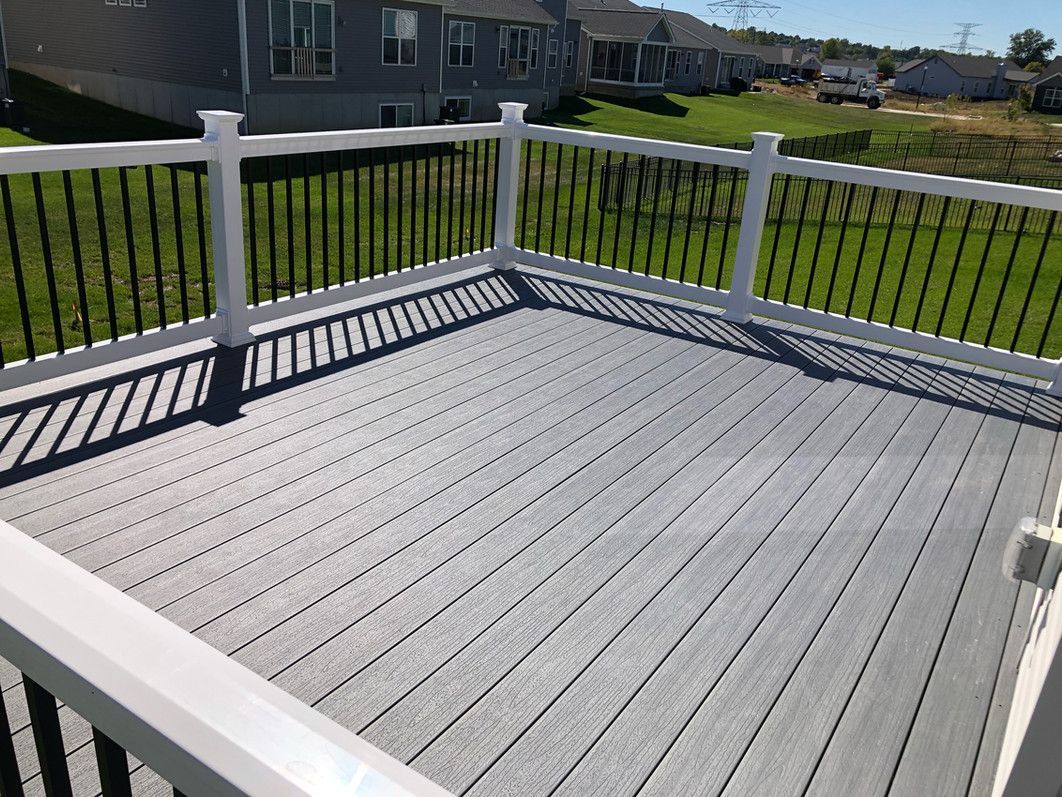 A gray composite deck with white railings and black balusters on a sunny day.