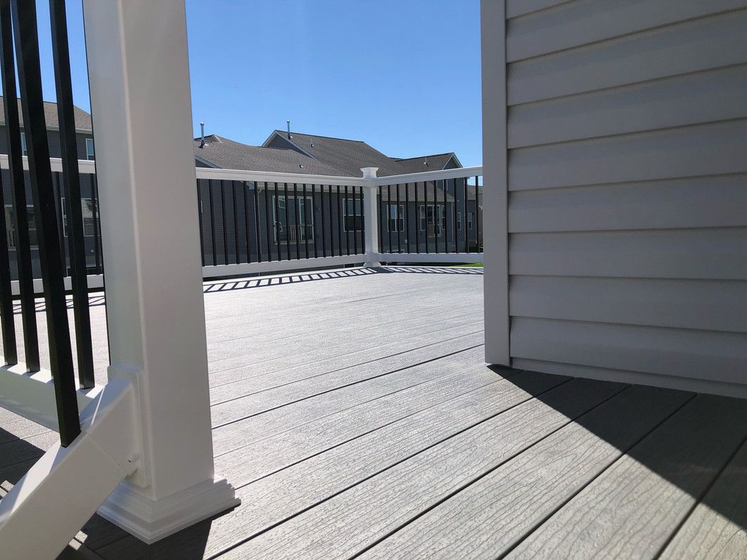 View from a deck with gray composite decking, white railings, and black balusters. Blue sky and houses in the background.