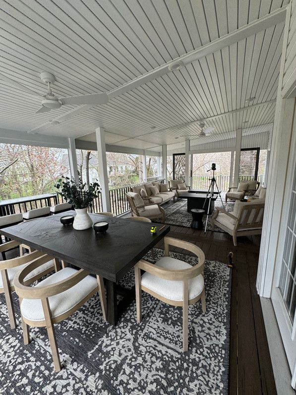 Covered porch with dark dining table, light chairs, and seating area with a patterned rug.