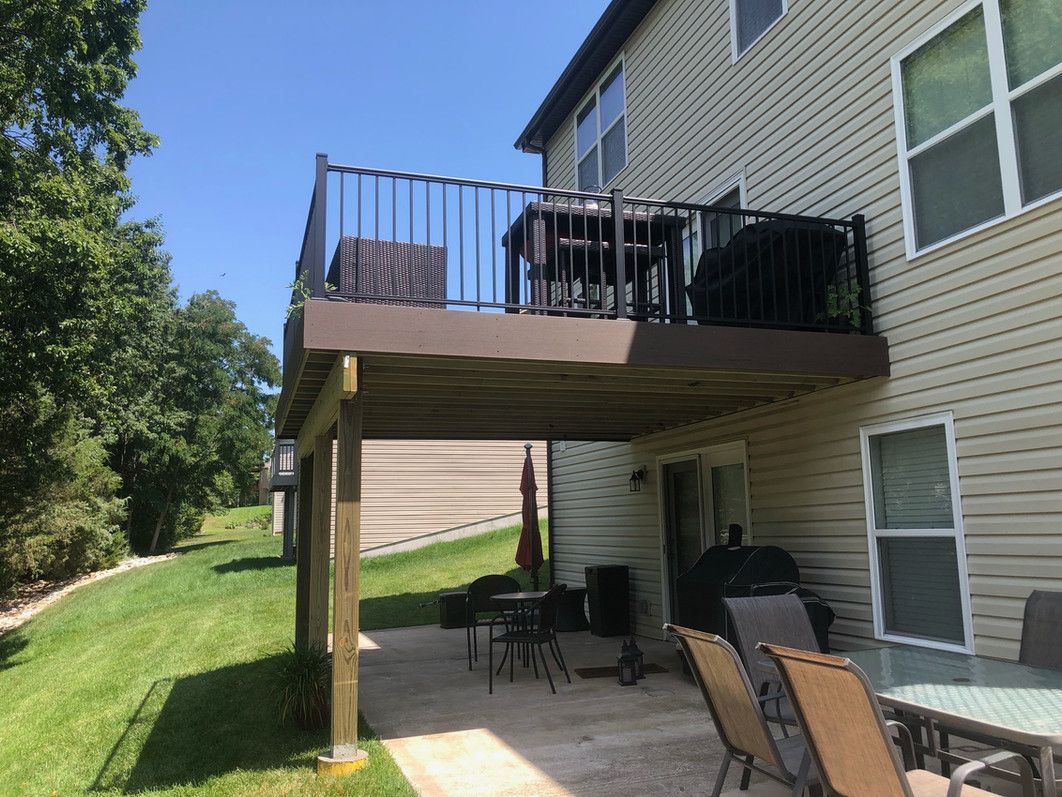 Two-story house with an elevated deck and a ground-level patio with outdoor furniture.