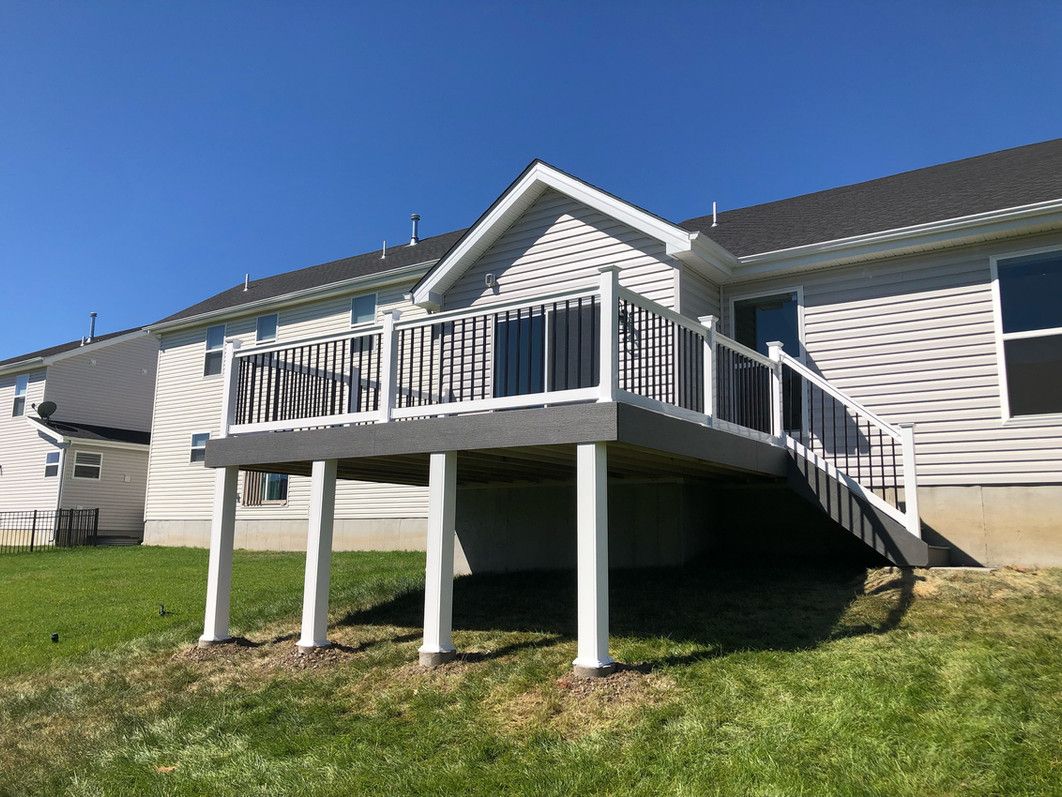 A gray composite deck with white railings and supports, attached to a light gray house.