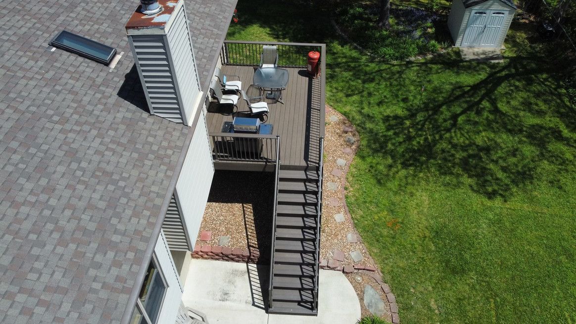 Overhead view of a house deck with stairs, furniture, a grill, and a grassy backyard.