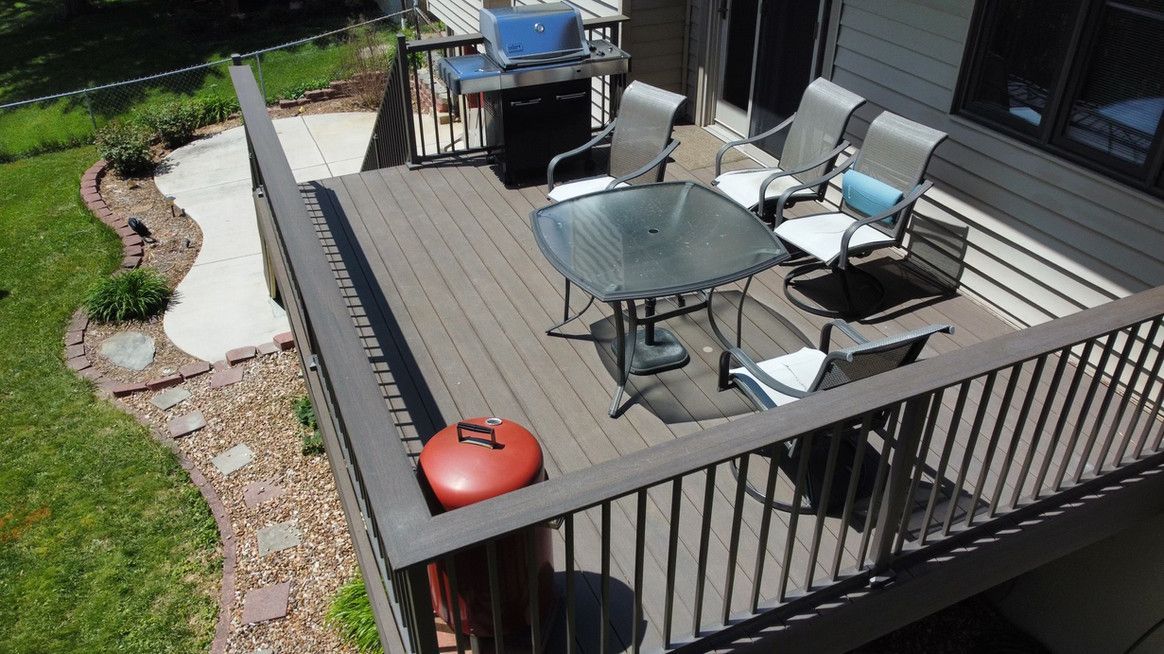 Wooden deck with patio furniture, grill, and red container; grass and walkway visible.