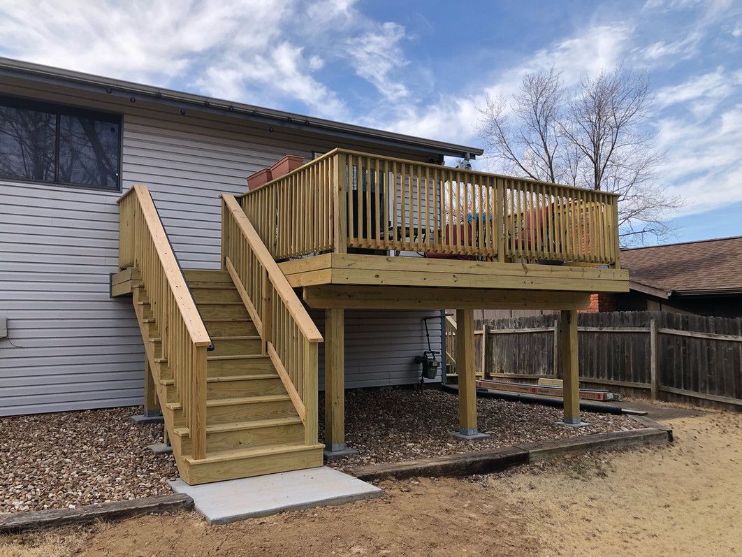 Wooden deck with stairs attached to a house; partially cloudy sky.