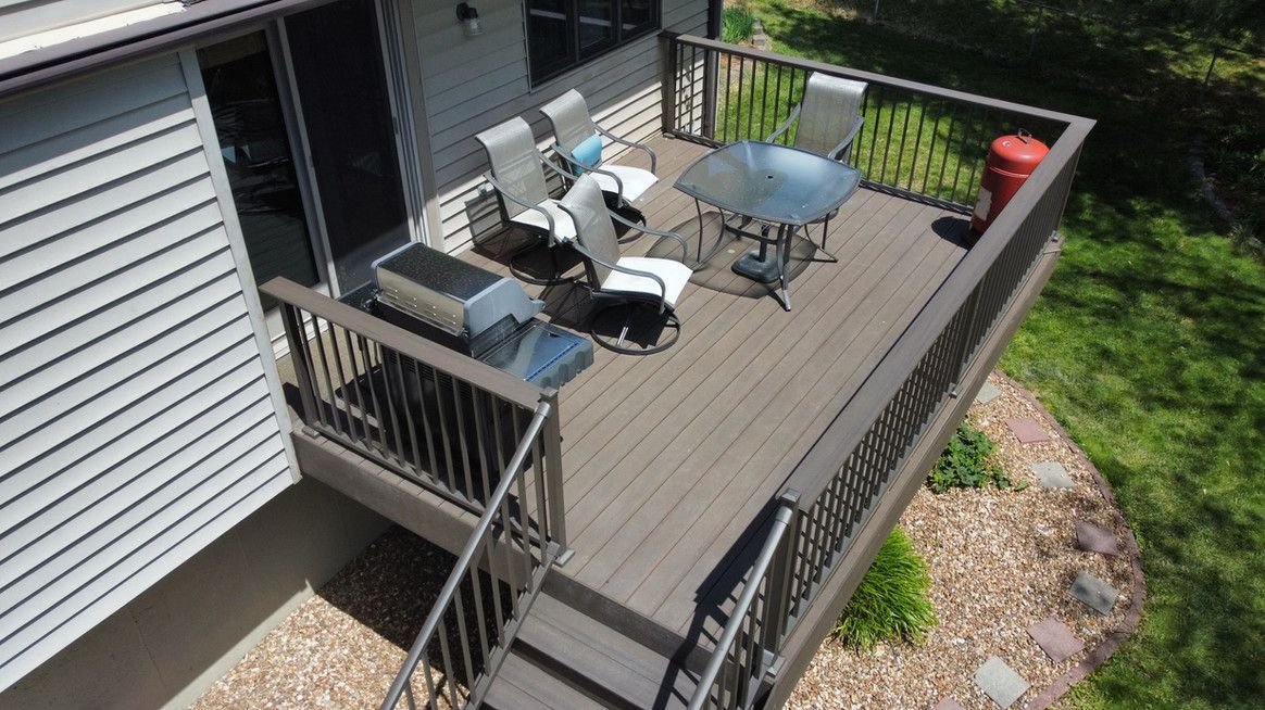 Wooden deck with chairs and table, next to a house, with steps leading down.