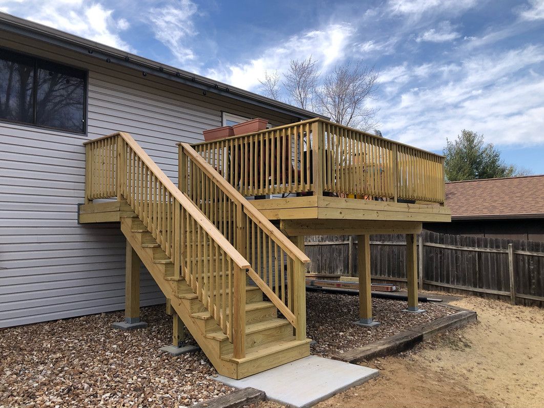 Wooden deck with stairs attached to a house. Cloudy blue sky.